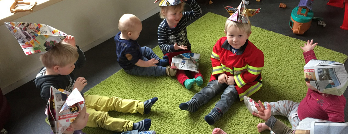 Kinderen met zelfgevouwen krantenhoedjes spelen samen op het groene kleed